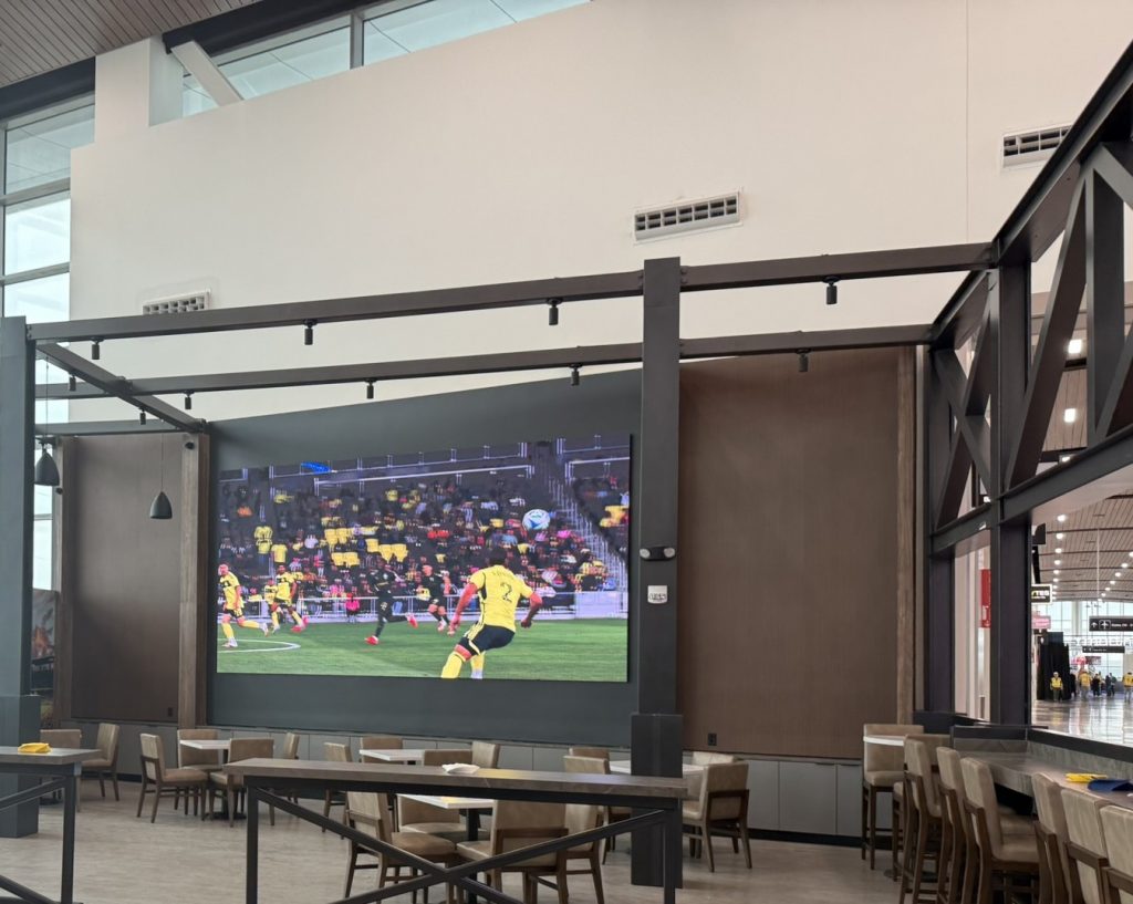 Large display showing a sports broadcast above a seating area.